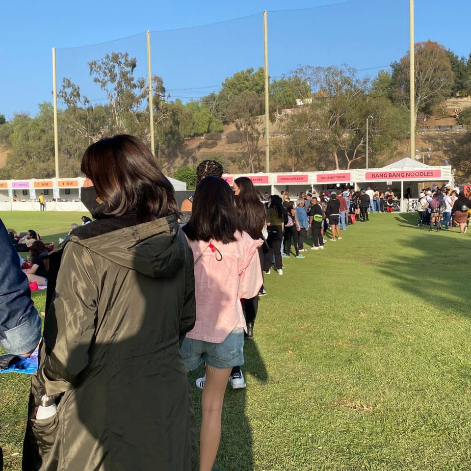 A long line of people waiting for Bang Bang Noodles at an outdoor event on a sunny day.