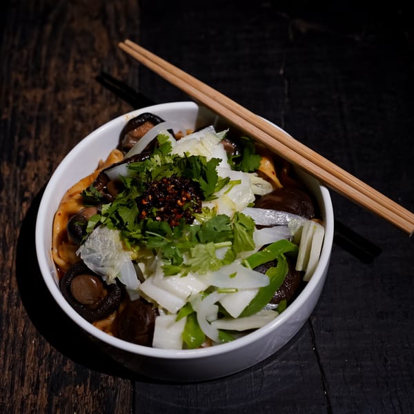 A bowl of Bang Bang Noodles with mushrooms, cabbage, cilantro, and chili oil, with chopsticks.