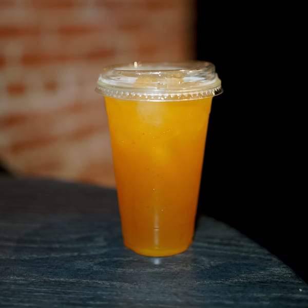 A vibrant orange drink in a clear plastic cup with a lid, sitting on a dark table.