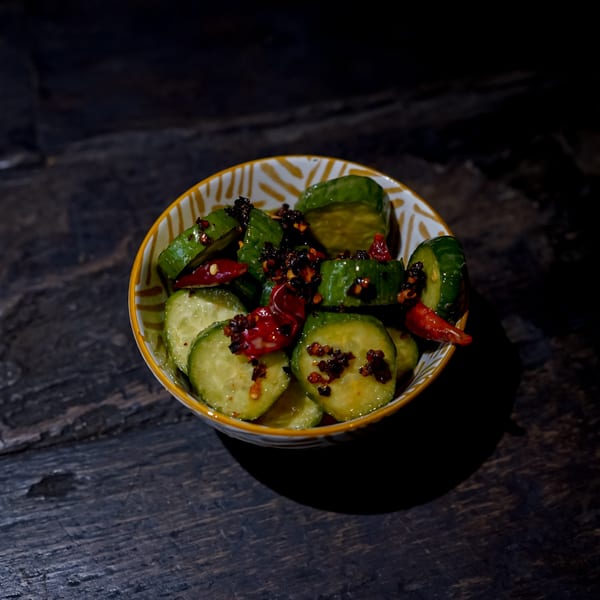 Bang Bang Noodles' spicy cucumber salad with chili oil and red peppers in a patterned bowl.
