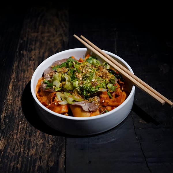 A bowl of Bang Bang Noodles with beef, green onions, and chili sauce, with chopsticks.