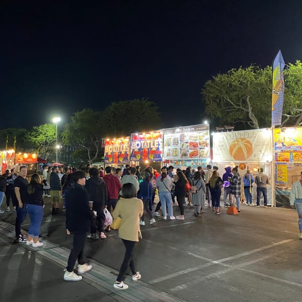 A bustling night market scene with numerous food stalls and a crowd of people.