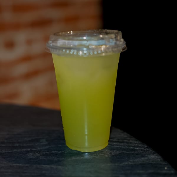 A vibrant yellow drink in a clear plastic cup with a lid sits on a dark table.