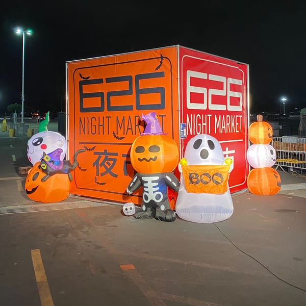 Inflatable Halloween decorations, including pumpkins, ghosts, and a witch cat, in front of a "626 Night Market" sign.