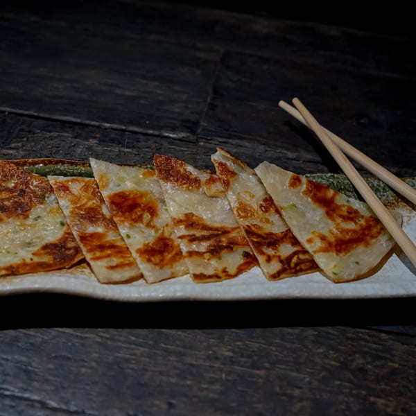 Crispy, golden-brown scallion pancakes, sliced into triangles, served on a white plate with chopsticks.