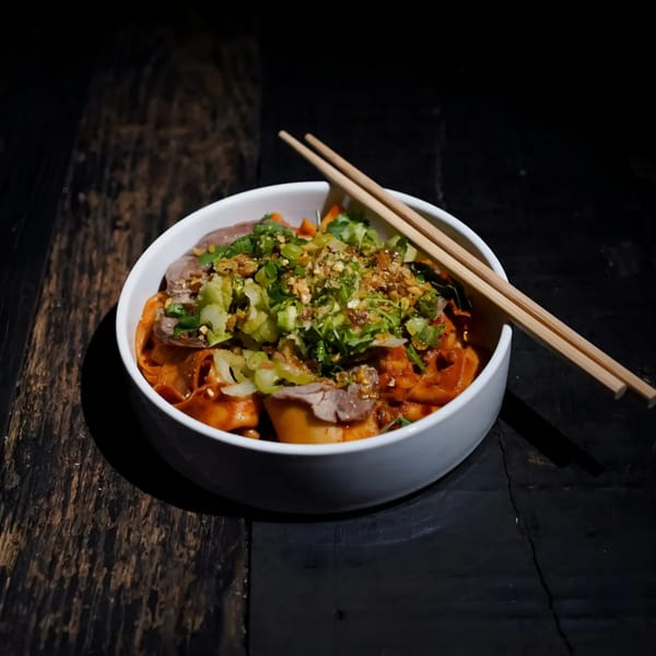 Bang Bang Noodles' spicy noodles with beef, green onions, and crushed peanuts in a white bowl.