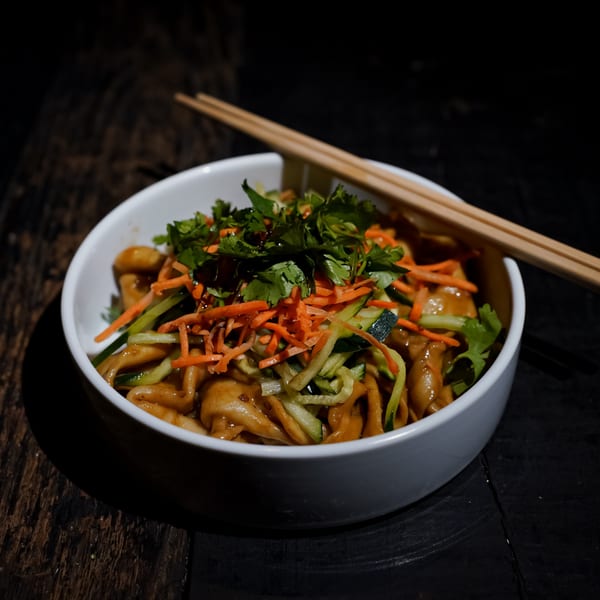 Bang Bang Noodles' Chinese noodles with shredded carrots, cucumbers, and cilantro in a white bowl.